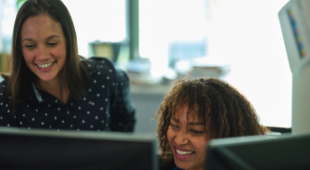 Two female EDF employees smiling whilst looking at computer monitors