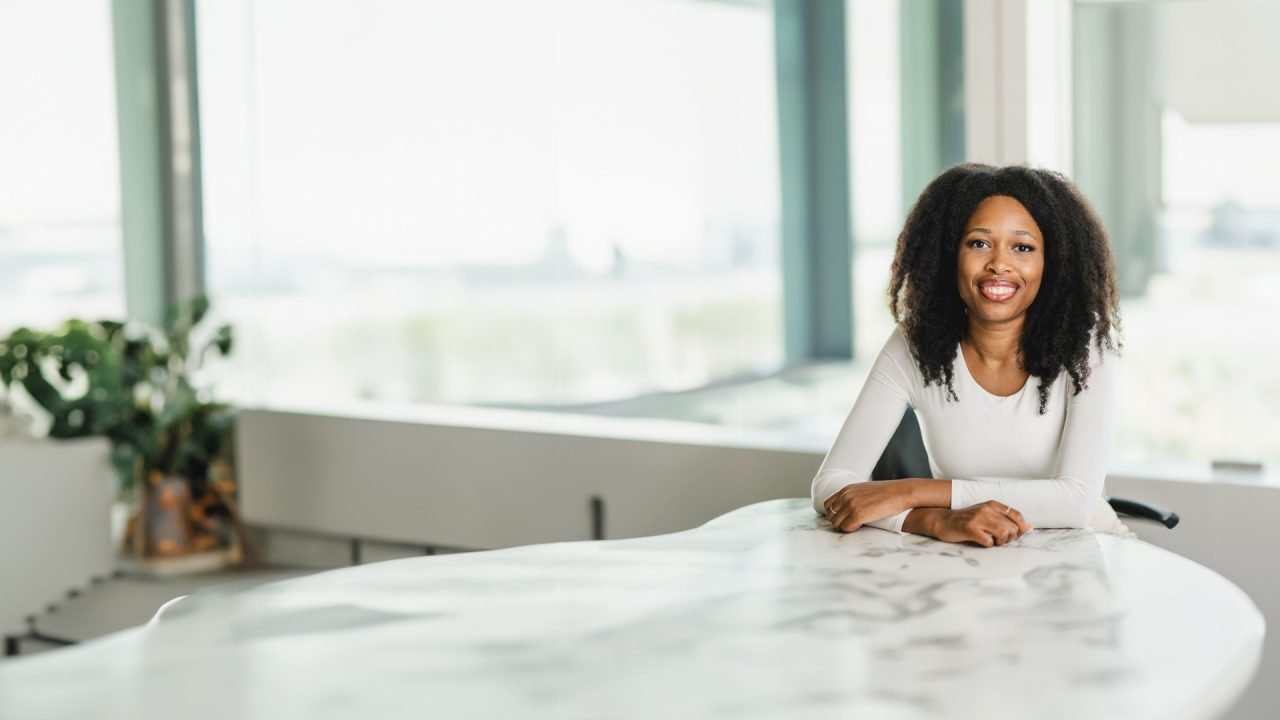 A woman with dark curly hair wearing a white top in an office environment
