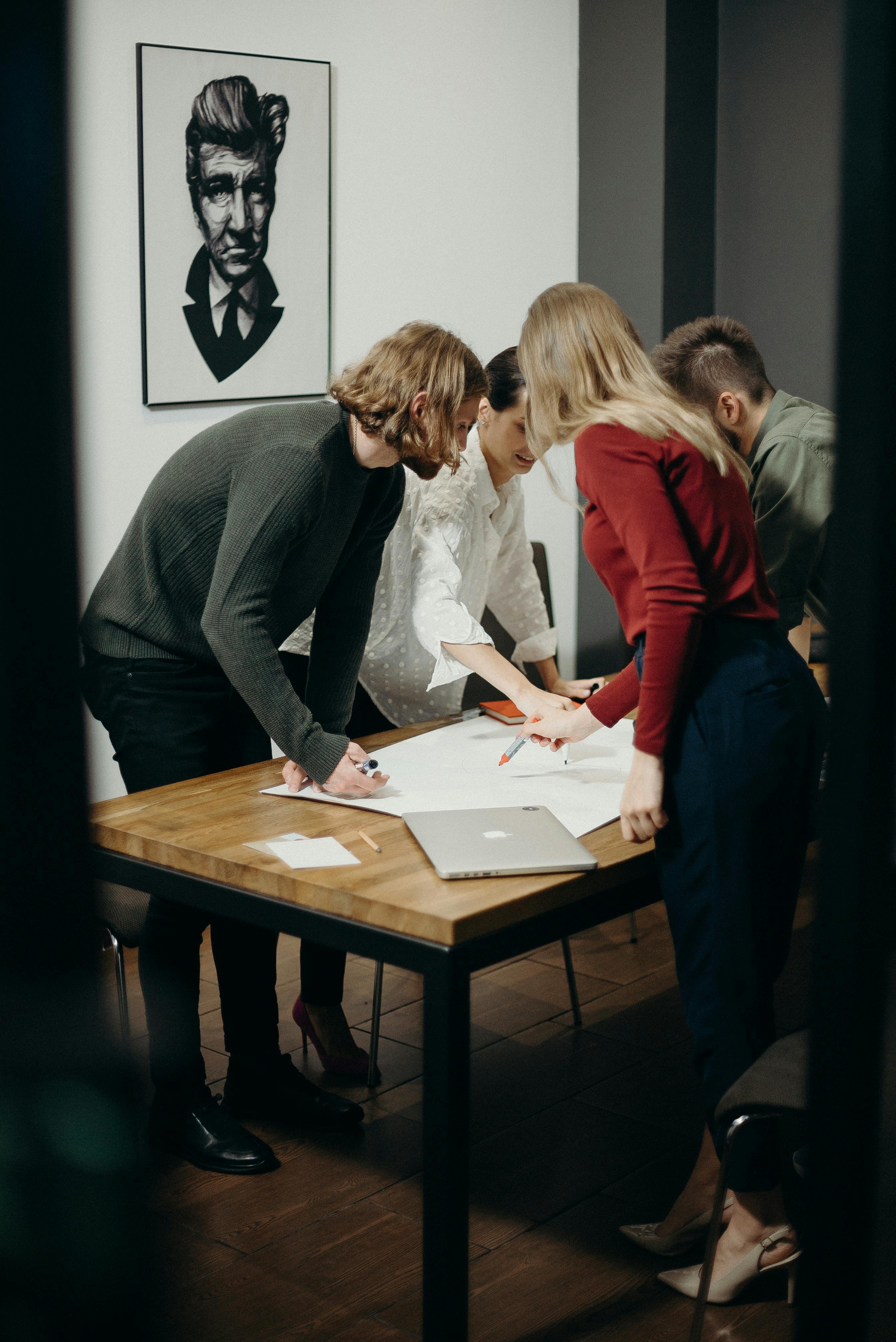 A group of people collaborating on a sheet on paper, leaning over a desk table.