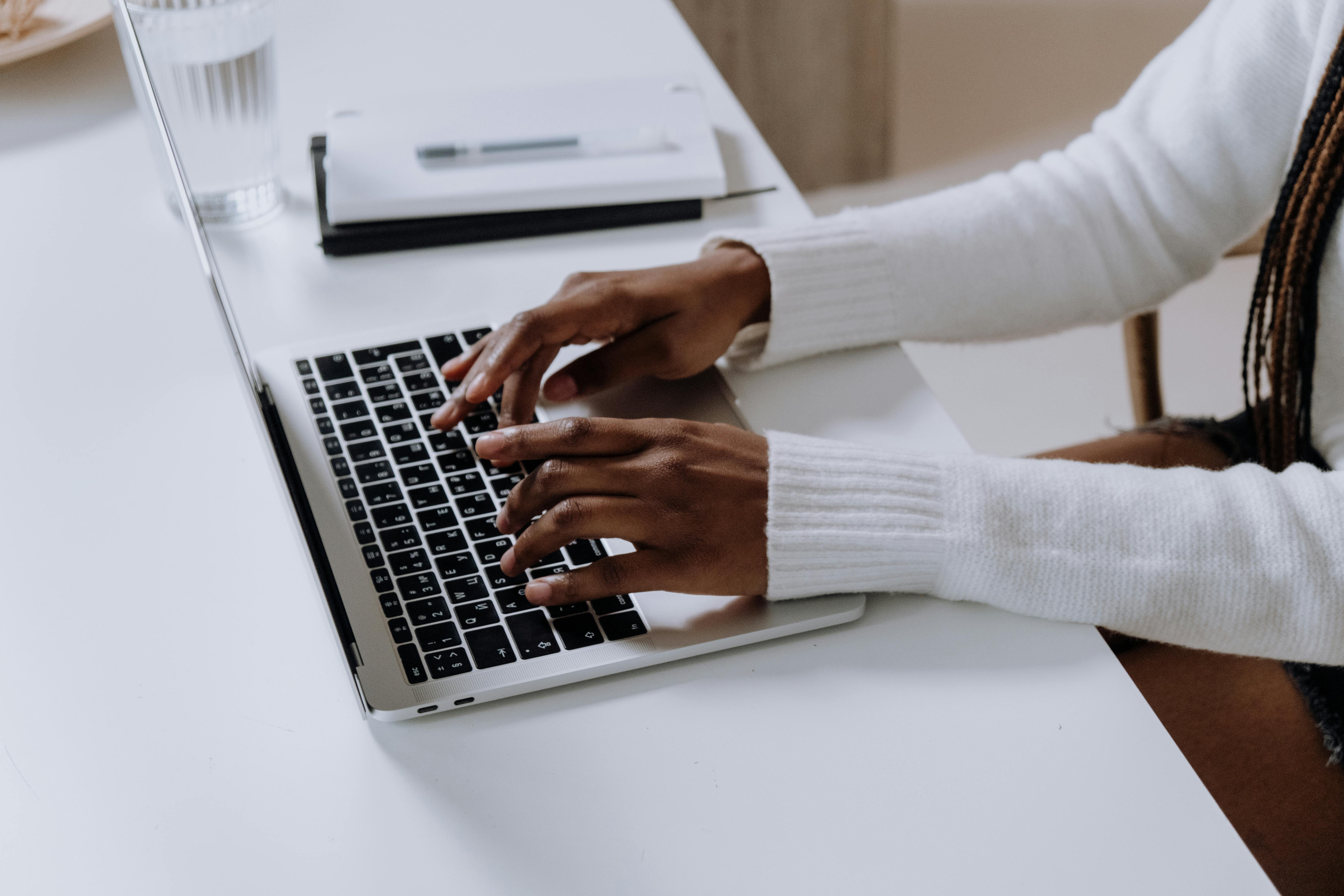 A woman wearing a long-sleeved white top typing on a laptop.